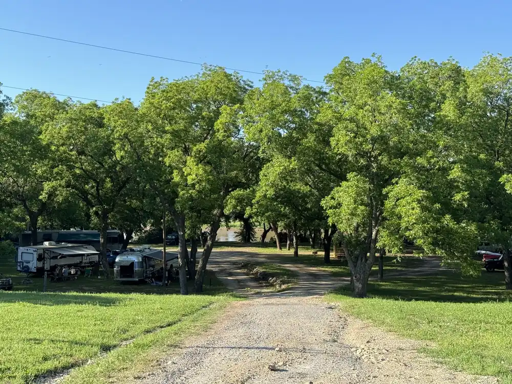 Tree-lined gravel drive entering Rivershire RV Resort in summer