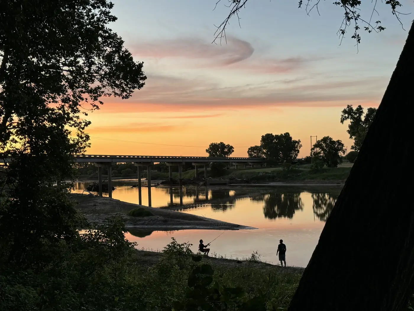 Two people fishing at sunset with bridge reflection on the Salt Fork River
